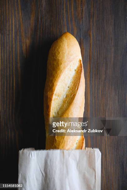 freshly baked bread in a paper bag or package, on a cutting board, on a brown wooden table, close-up. copy space for text. the concept of organic farming food, no plastic. - flute stockfoto's en -beelden