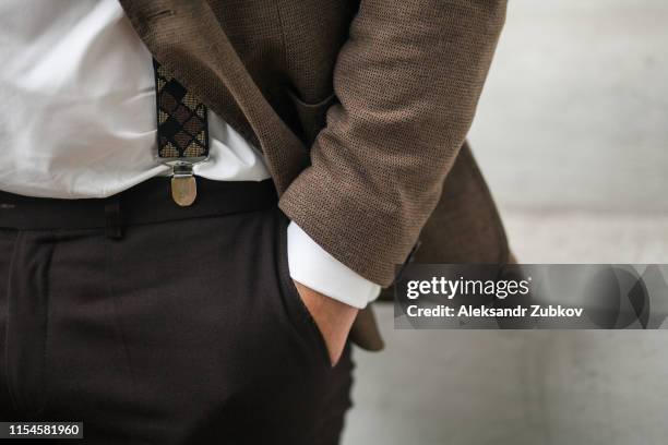 a man's hand in the pocket of brown stylish pants close-up on a white background. successful young man, businessman, entrepreneur in an expensive business brown suit, white shirt and suspenders. - bruin pak stockfoto's en -beelden