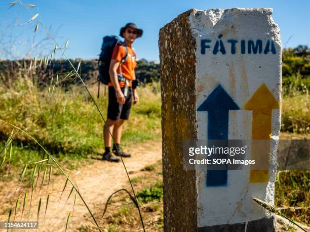 Pilgrim stands next to a stone with a yellow and a blue arrow indicating the way to Fatima. The Camino de Santiago is a large network of ancient...