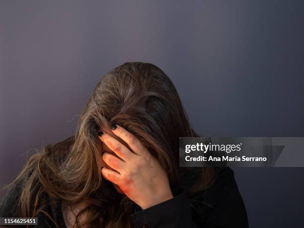 a woman with gray eyes and long hair with blood on her hand touching her face - victim advocacy stock pictures, royalty-free photos & images