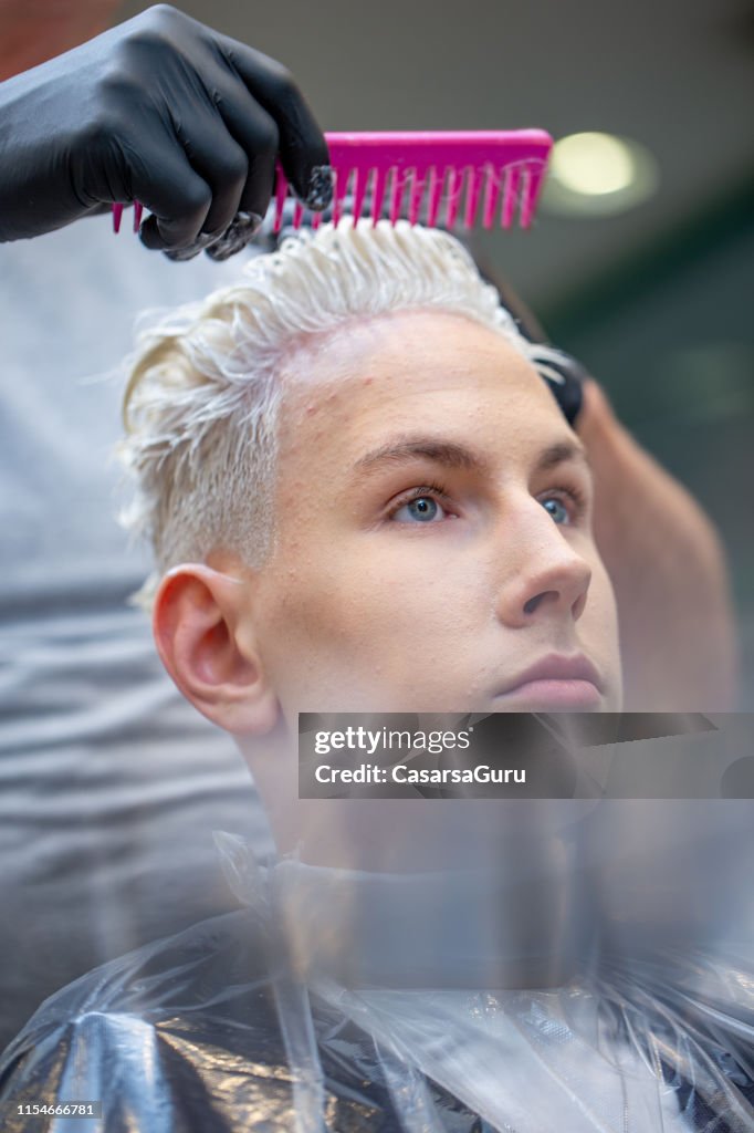 Retrato do homem adulto novo com cabelo descorado no tratamento do cabelo e no salão de beleza