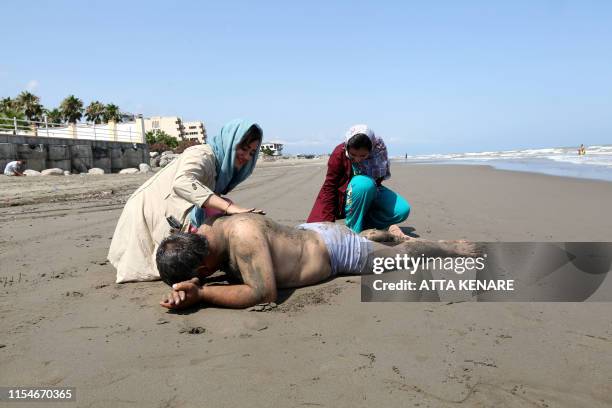 An Iranian woman puts sand sand on her father's back on the beach in the Caspian Sea city of Izadshahr, in the northern Mazandaran province, on July...