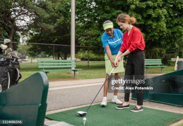 the active 77-years-old senior african-american woman teaching the 18-years-old caucasian girl to play golf. - coach travel stock pictures, royalty-free photos & images