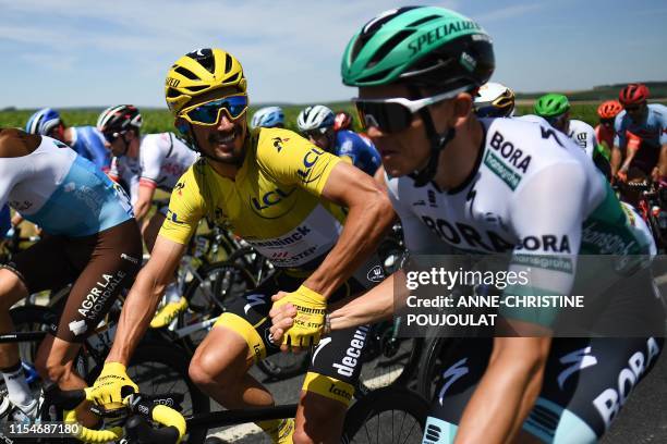 France's rider Julian Alaphilippe , wearing the overall leader's yellow jersey, and Austria's rider Gregor Muhlberger hold hands as they ride side by...