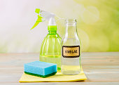 Chemical free home cleaner products concept. Using natural destilled white vinegar in spray bottle to remove stains. Tools on wooden table, green bokeh background, copy space.