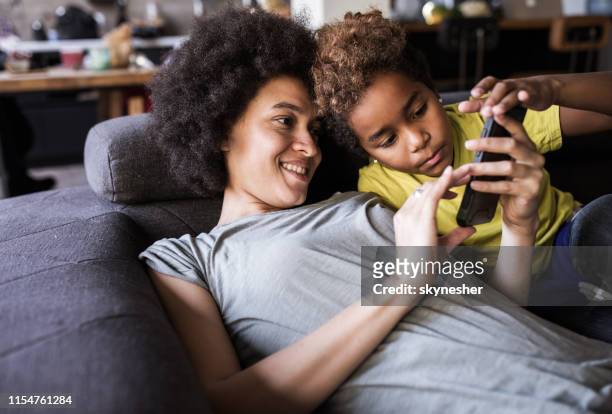 african american mother and daughter using cell phone on sofa at home. - text messaging mother stock pictures, royalty-free photos & images