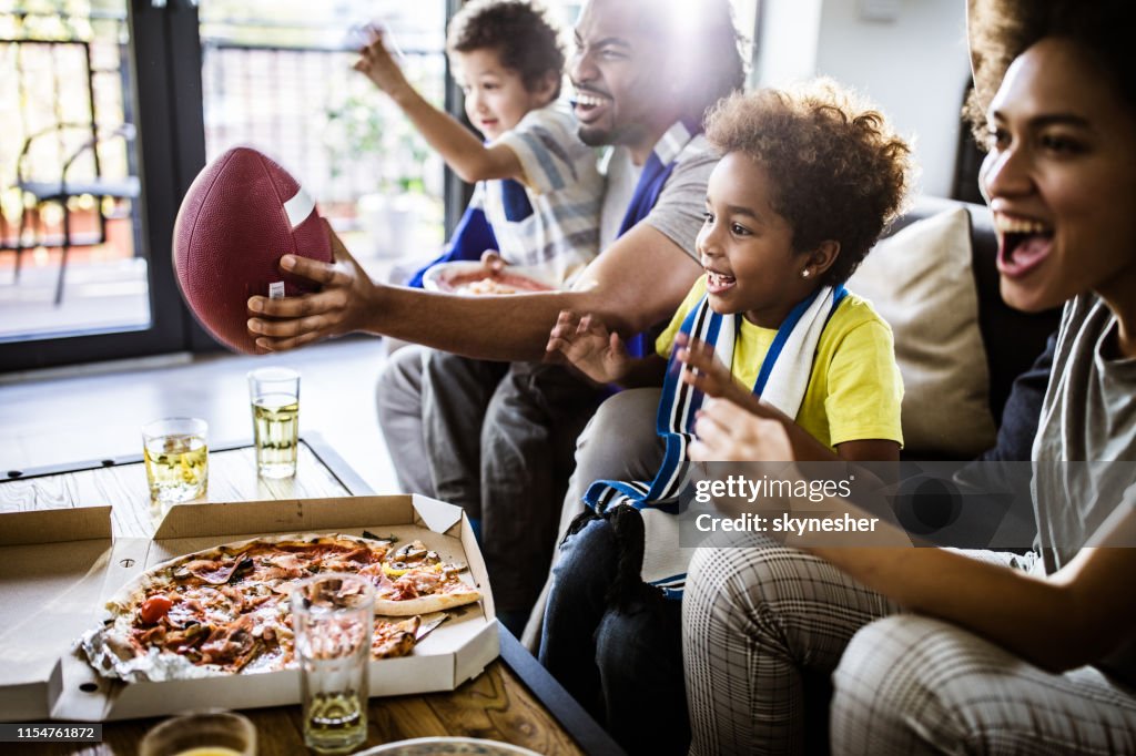 Cheerful black family cheering while watching rugby match on TV at home.