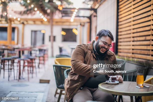 bearded man drinking coffee in a cafe garden - overweight man stock pictures, royalty-free photos & images