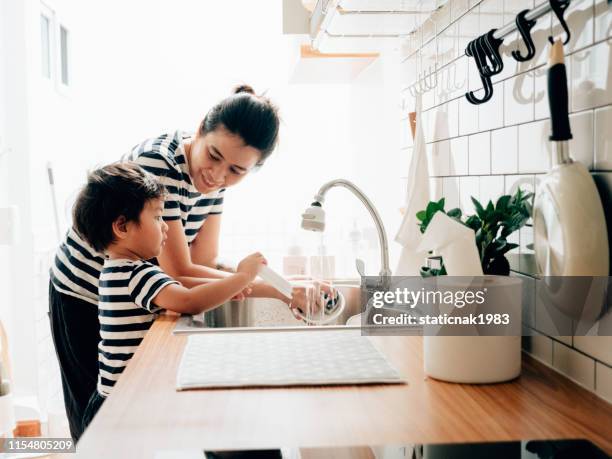 petit bébé garçon essuyant des plats propres avec sa mère. - child washing hands photos et images de collection