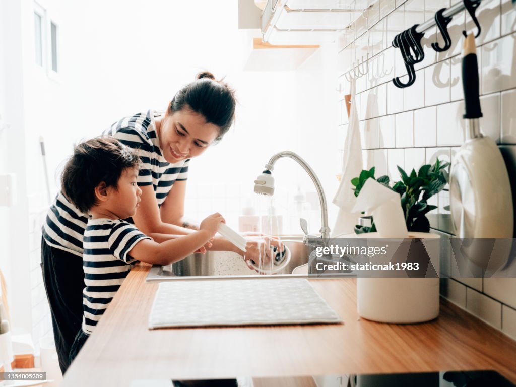 小さな男の子は彼の母親と一緒にきれいな料理を拭きます。