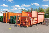 orange waste compactors are standing on a factory site with other waste containers next to them