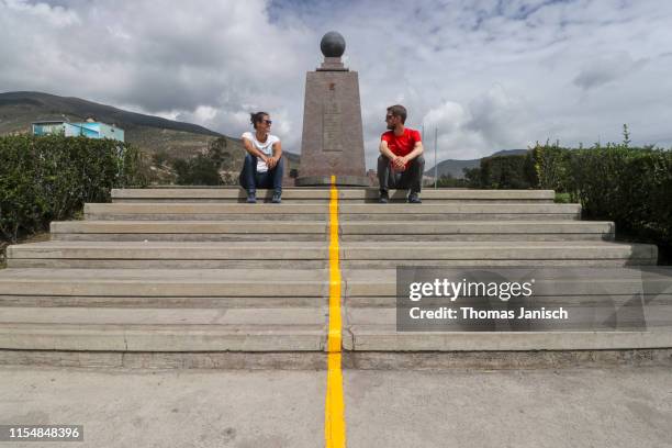 two people sitting at the yellow line dividing the two hemispheres at the monument to the equator, ciudad mitad del mundo, ecuador - equator line stock pictures, royalty-free photos & images