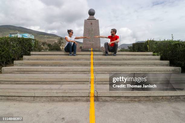two people sitting at the yellow line dividing the two hemispheres at the monument to the equator, ciudad mitad del mundo, ecuador - äquator stock-fotos und bilder