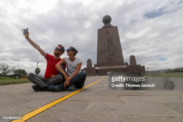 couple taking a selfie at the yellow line dividing the two hemispheres at the monument to the equator, ciudad mitad del mundo, ecuador - quito stock-fotos und bilder
