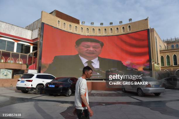 This photo taken on June 4, 2019 shows a man walking past a screen showing images of China's President Xi Jinping in Kashgar in China's northwest...
