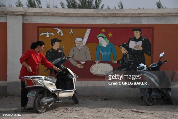 This photo taken on June 2, 2019 shows a Uighur woman beside a propaganda painting showing soldiers meeting with a Uighur family, outside a military...