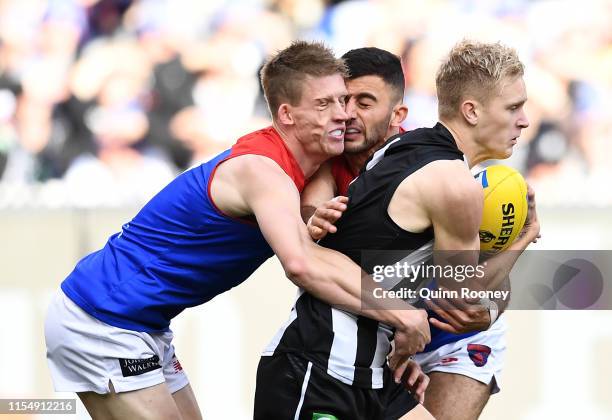 Christian Salem and Sam Frost of the Demons collide heads whilst tackling Jaidyn Stephenson of the Magpies during the round 12 AFL match between the...