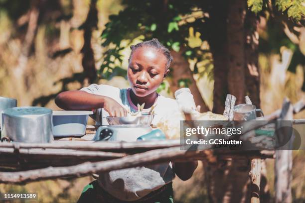 jeune femme africaine occupée dans un village exécutant des tâches courantes - makeshift photos et images de collection