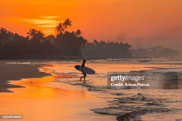 surfer at sunrise on the shores of the indian ocean - indonesia surfing imagens e fotografias de stock