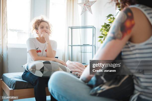 young woman sitting on the bed and listening to her friend - friends serious stock pictures, royalty-free photos & images