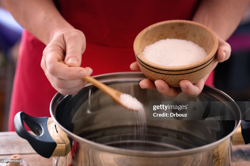 Pasta cooking - chef puts sea salt into boiling pot, close up