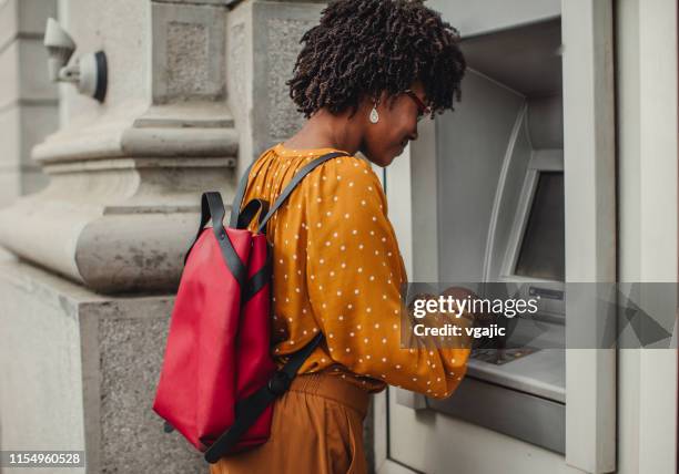 woman making a cash withdrawal at an atm - atm cash stock pictures, royalty-free photos & images