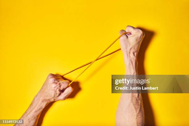 two hands twisting yellow cord on a bright yellow backdrop - elastisch weefsel stockfoto's en -beelden