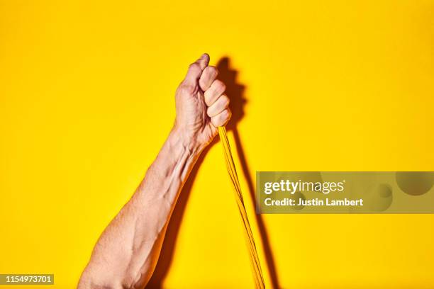 one hand pulling twisted yellow cord upwards on a bright yellow backdrop - elastisch weefsel stockfoto's en -beelden