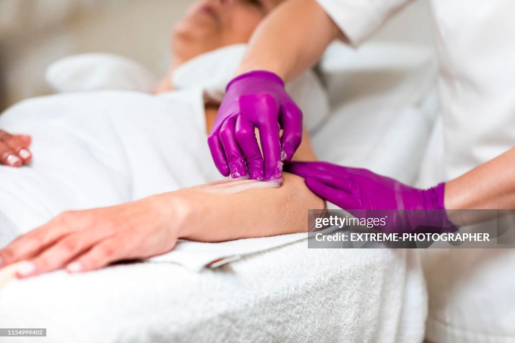 Technician using a  sugar wax to remove hair from a female's arm