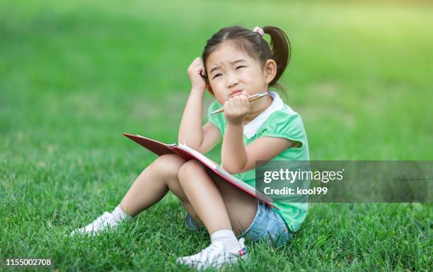 schattig klein meisje leren op het gazon - zich op het hoofd krabben stockfoto's en -beelden