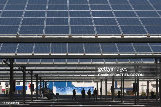 People walk under solar panels on September 19, 2010 during the inauguration of a solar panel installation on the car park of French auto maker PSA...