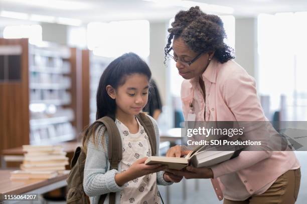 成熟した成人司書は、女の子が本で情報を見つけるのに役立ちます - librarian ストックフォトと画像