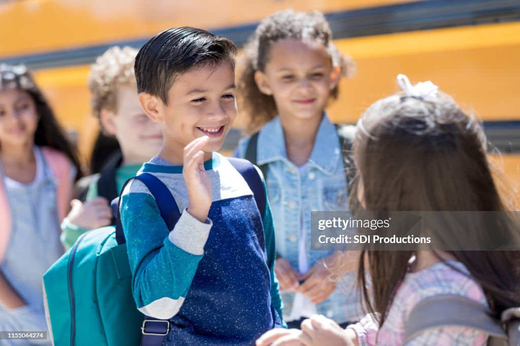 Schoolboy shyly waves at a girl at the bus stop