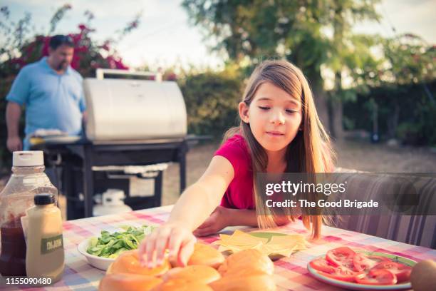 girl reaching for hamburger bun at backyard barbecue - backyard grilling stockfoto's en -beelden