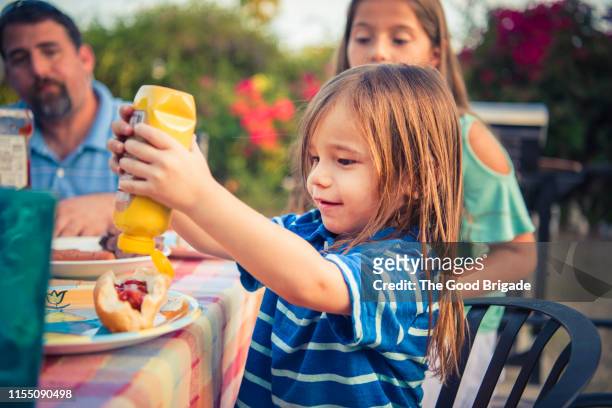 boy squeezing mustard on hot dog - moutarde assaisonnements et vinaigrettes photos et images de collection