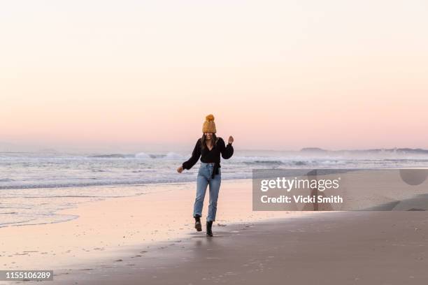 young asian lady dressed for winter walking on the beach at sunrise - australia winter stock-fotos und bilder