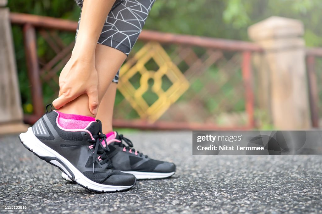 Close-up Asian woman standing on road holds her ankle injury after jogging