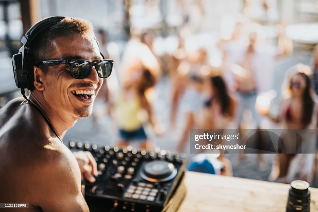 Happy male DJ playing music on a beach party.