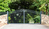 Metal driveway property entrance gates set in brick fence with garden trees  in background