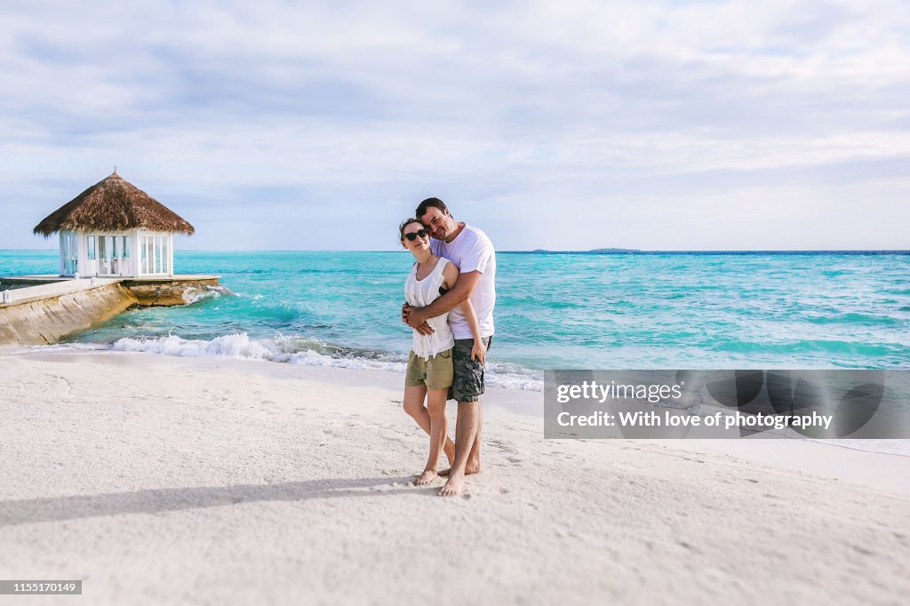 Romasntic couple in Maldives walking on the beach hugging and cuddling, love and romance, romantic getaway, honeymoon, loving couple, romance in Maldives, love and ocean, just for two, ocean waves, island vibes, romantic holiday, caucasian happy couple in