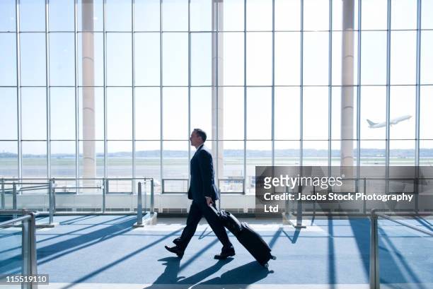 caucasian businessman pulling luggage in airport - business journey stock pictures, royalty-free photos & images