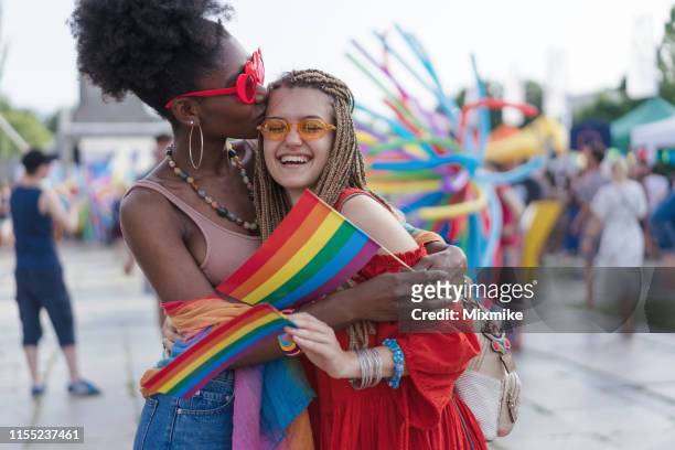junge frauen umarmen und küssen bei der liebesparade - pride fest stock-fotos und bilder