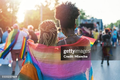 Pareja de mujeres jóvenes abrazando con bufanda de arco iris en el evento del orgullo Pareja de mujeres jóvenes abrazando con bufanda de arco iris en el evento del orgullo