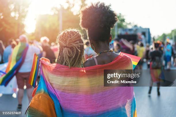 young female couple hugging with rainbow scarf at the pride event - lésbica imagens e fotografias de stock