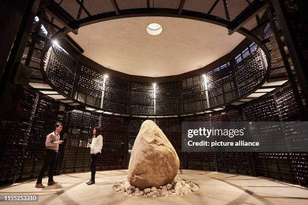 July 2019, Argentina, San Carlos: Two visitors drink wine surrounded by wine bottles in the wine cellar of Piedra Infinita wine. The Argentinian...