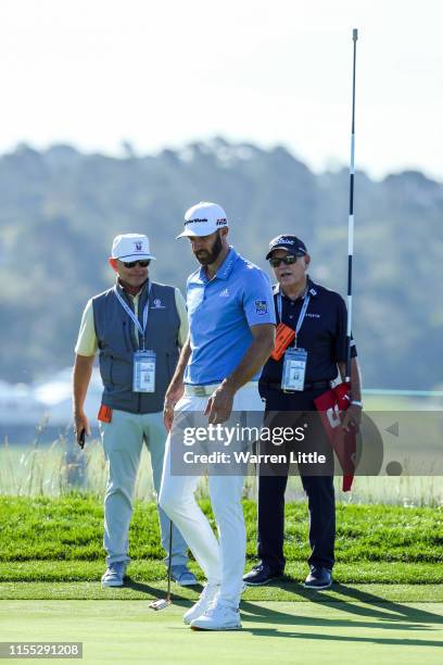 Dustin Johnson of the United States lines up a putt as player instructor, Butch Harmon, and player manager, David Winkle, look on during a practice...