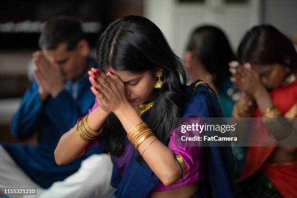 a beautiful indian family sits in their living room one afternoon praying together. they are celebrating and giving thanks during the holiday diwali. they are bonding as they are donned in traditional clothing. - hinduism photos stock pictures, royalty-free photos & images