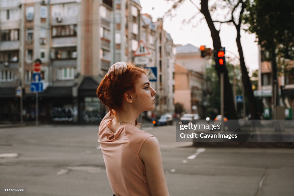Young redheaded woman holding hair while standing in city street