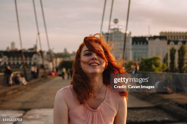 young woman with red hair walking on bridge in city - red dress stock-fotos und bilder