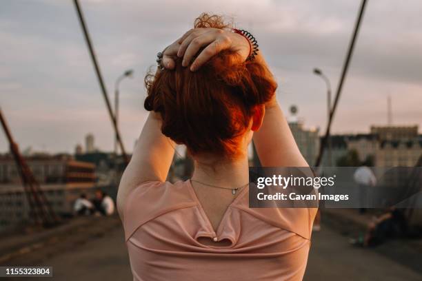 back view of redhead woman holding hair while standing on bridge - red blouse stock pictures, royalty-free photos & images